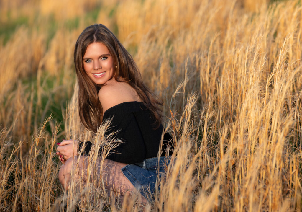 senior portrait sitting in a field during golden hour