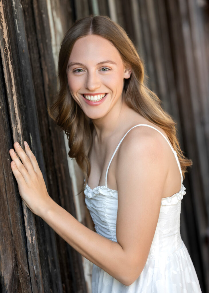 High school senior Spring season brown hair fair complexion in field at sunset hair down hands in front on barn wall white shirt