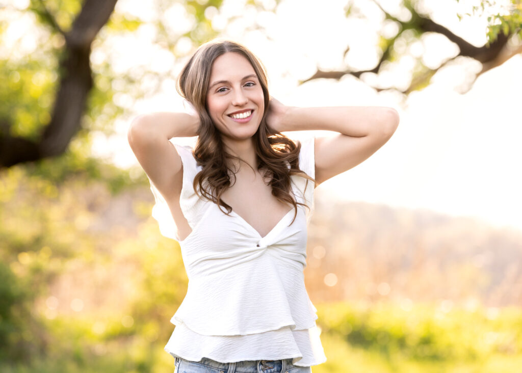 High school senior Spring season brown hair fair complexion in field at sunset hands on head