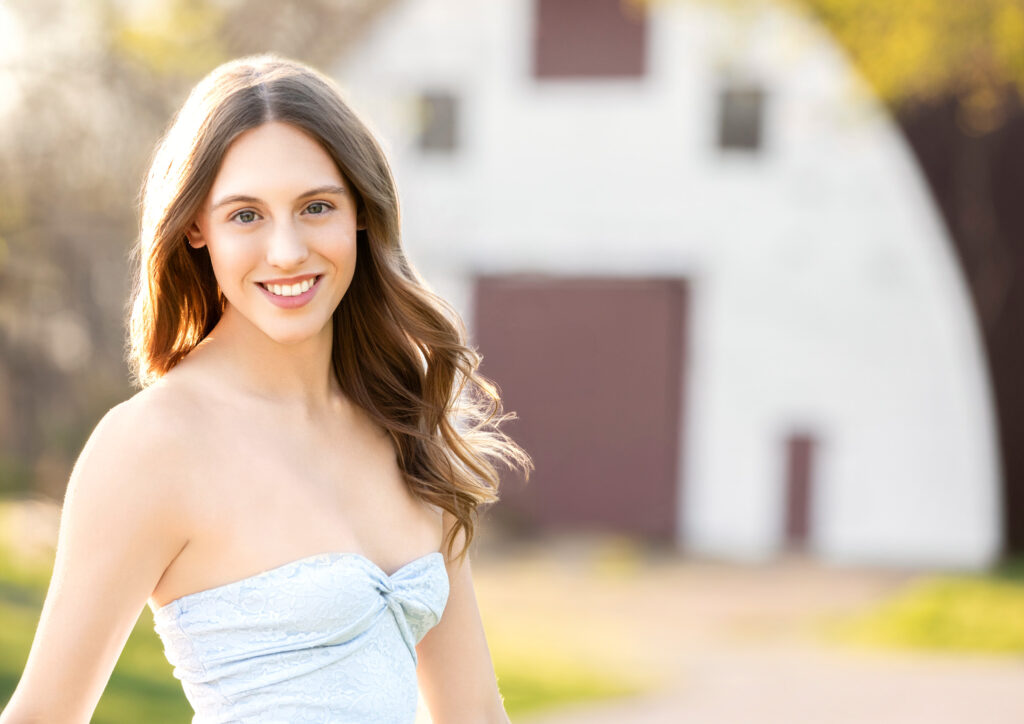 High school senior Spring season brown hair fair complexion white barn in background light blue strapless top