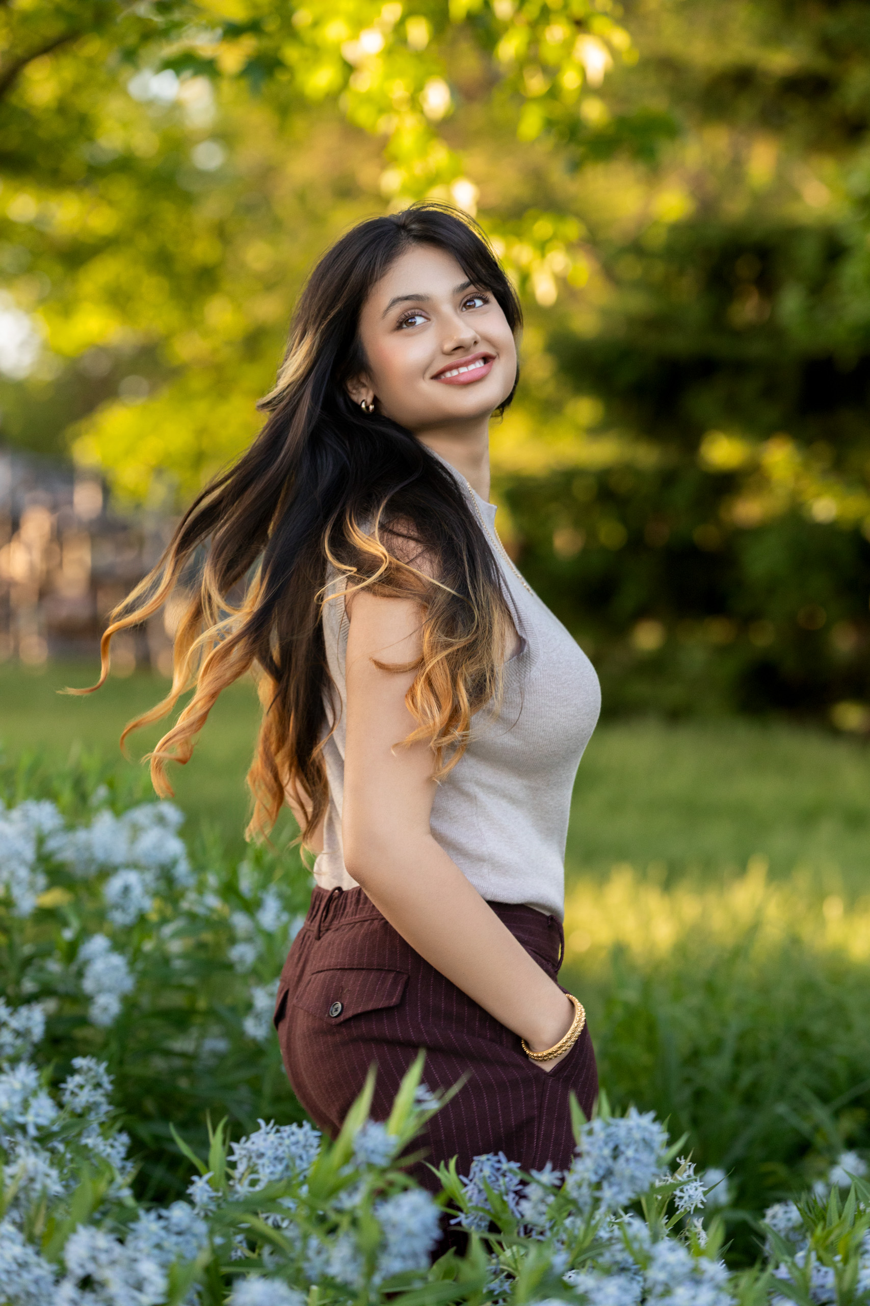 High school senior in a tan top and brown pants in a field of blue flowers long flowing brown hair