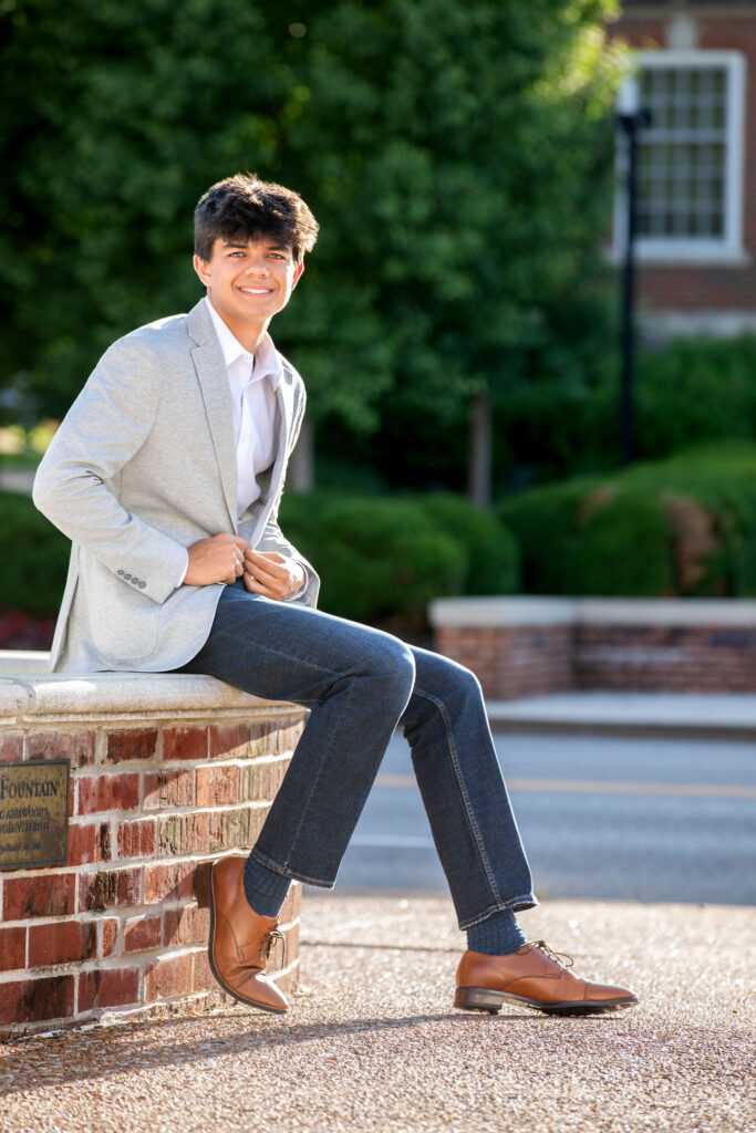 High school senior sitting on brick wall in gray blazer and jeans 