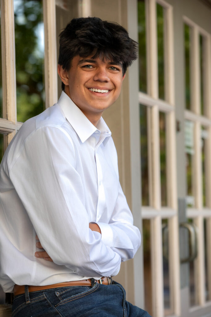 High school senior sitting on window sill outside in white oxford