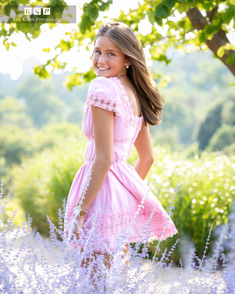 High school senior in a flower field looking over shoulder in pink dress