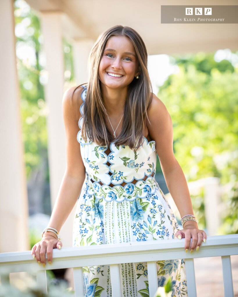 High school senior on porch looking over railing in blue floral dress