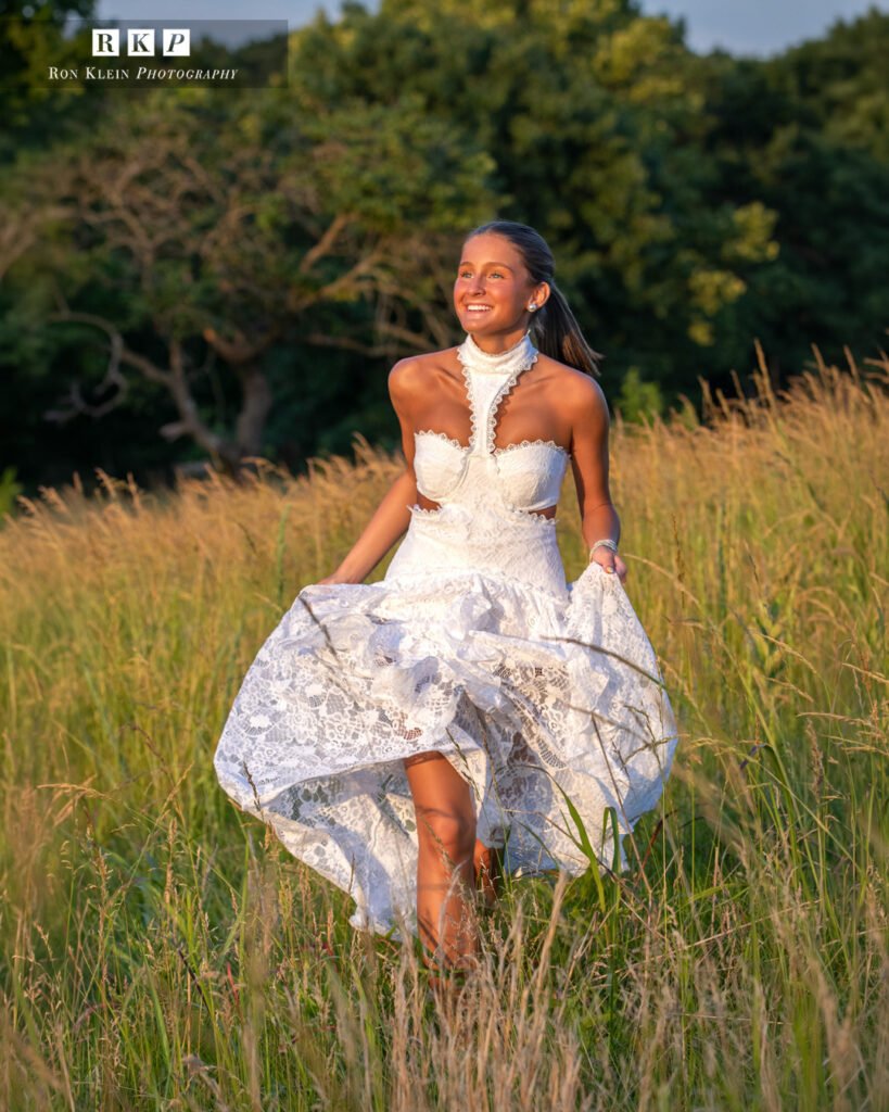 High school senior golden hour white dress in grassy field running hands holding dress