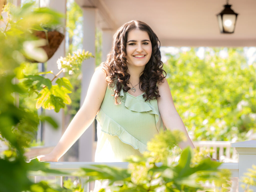 High School Senior Spring Session. Green dress. Standing on front porch. Long brown curly hair.