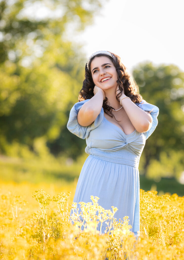 High School Senior Spring Session. Standing in a field of yellow flowers, blue dress, curly hair.