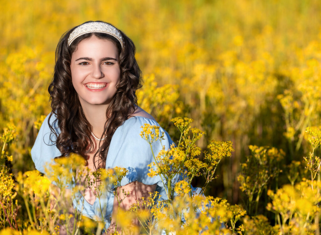 High School Senior Spring Session. Sitting in a field of yellow flowers, blue dress, curly hair.