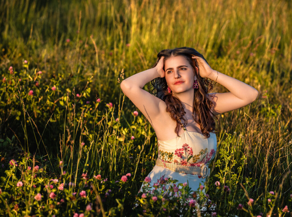 High School Senior Spring Session. Standing in a field of pink flowers, hands in hair, floral dress curly hair