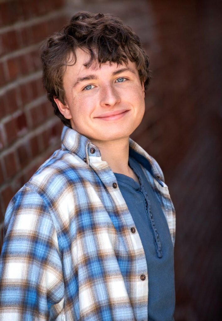 High school senior leaning against a brick wall plaid shirt