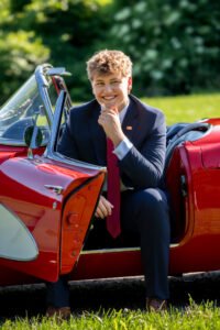 Red sports car high school senior portrait teen in a suit red tie outside