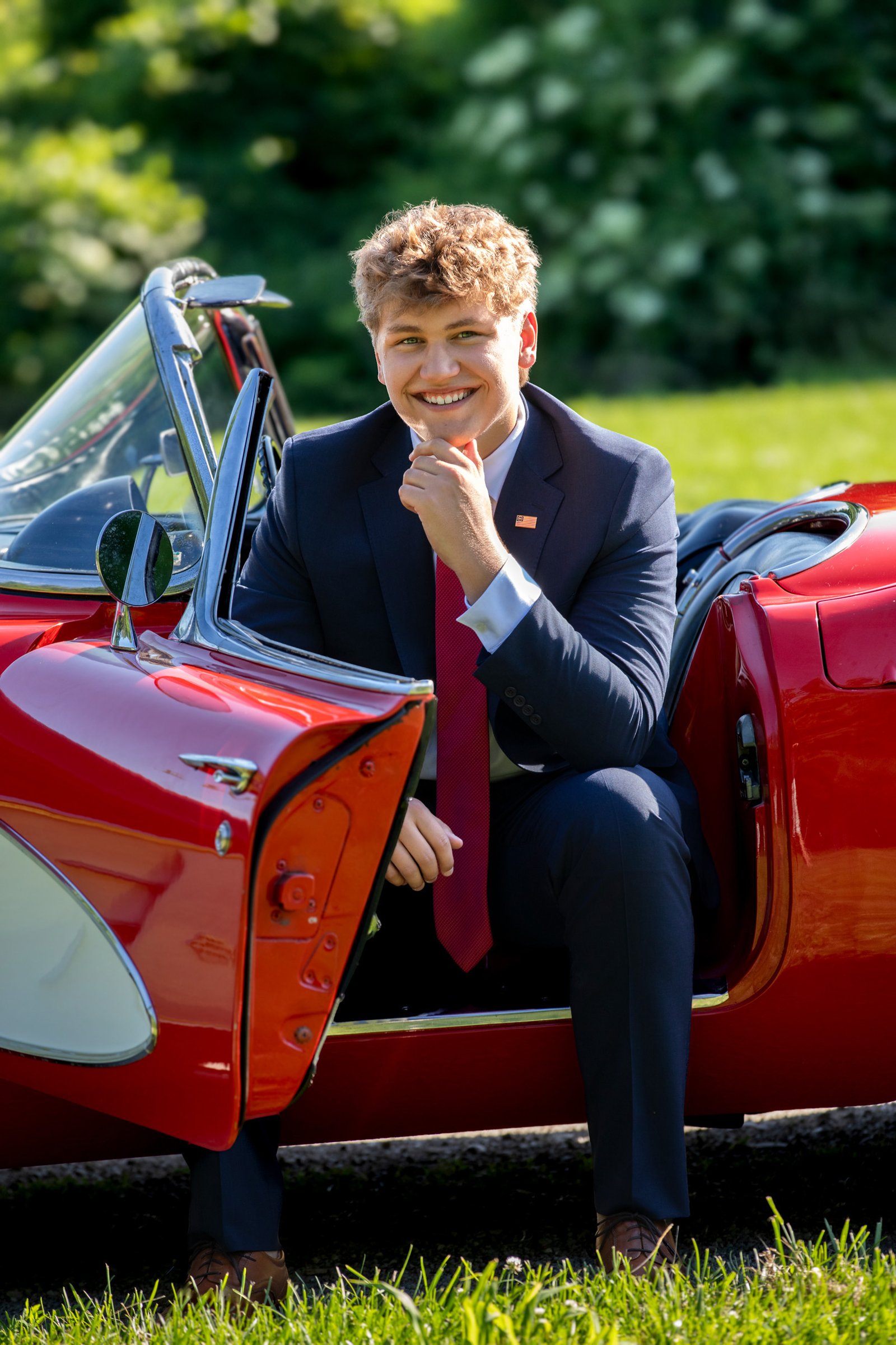 Red sports car high school senior portrait teen in a suit red tie outside