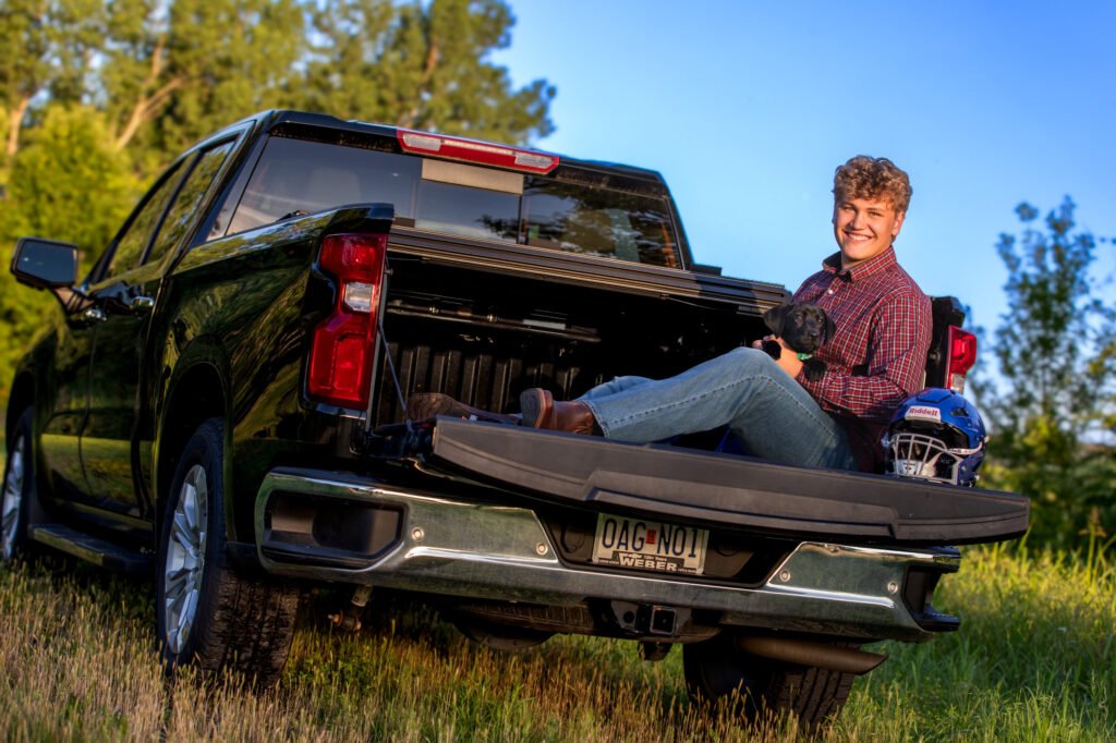 High school senior sitting in the back of a pickup truck with black lab puppy and football helmet