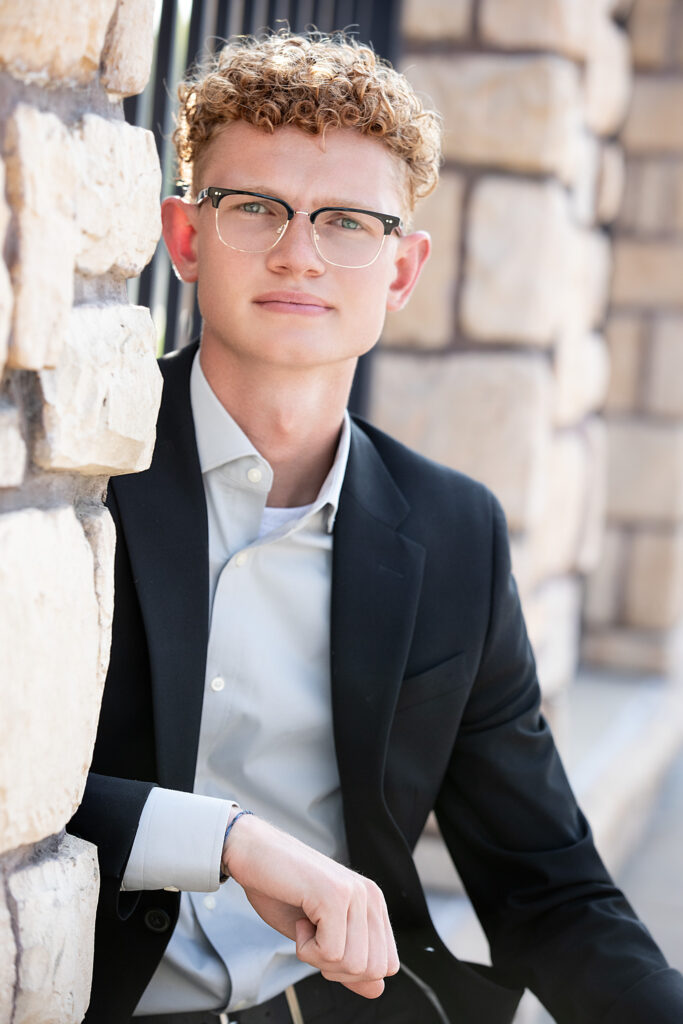High school senior sitting on a rock wall in downtown Wildwood, MO in a suit looking at camera