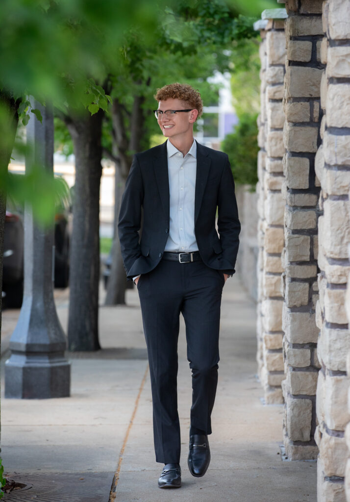 High school senior walking on sidewalk in downtown Wildwood, MO in a suit looking away from the camera