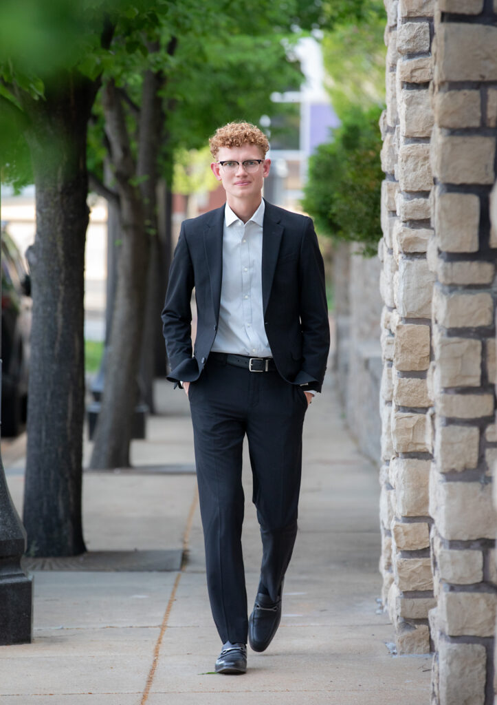 High school senior walking on sidewalk in downtown Wildwood, MO in a suit looking at camera