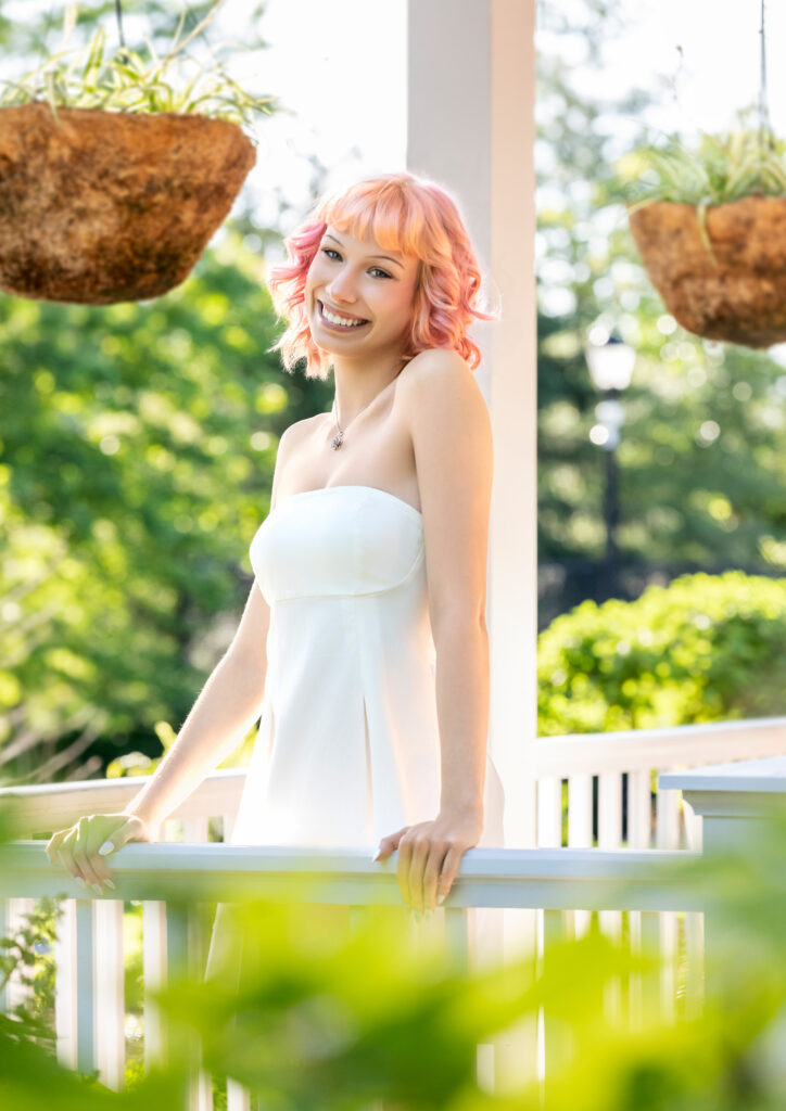 High school senior in white dress on white porch and pink hair